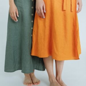 Two women stand barefoot on a white floor, showcasing colorful dresses in a minimalist fashion style.